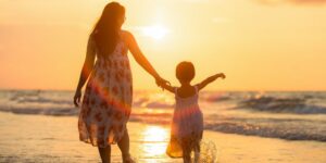 A mother holding her child's hand on the beach at sunset