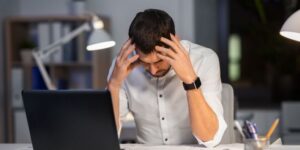 A man stressed and hunched over a laptop